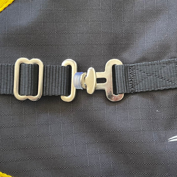 Close-up of the Ram Rug | Waterproof showing its black fabric strap with a silver buckle and fastener, securely attached to the textured black blanket with yellow trim visible along the left edge.